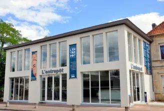 L'Entrepôt du Haillan, a modern white building with large glass windows and blue signage, located in Bordeaux, serving as a cultural and exhibition venue.