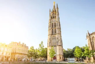 Pey-Berland Tower, a 15th-century Gothic bell tower in Bordeaux, featuring ornate spires and a golden statue on top, surrounded by historic buildings and trees.