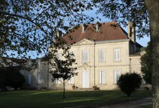 Château Mangot in Bordeaux, an elegant cream-colored stone mansion with red tile roof, surrounded by lawn and trees, featuring a symmetrical facade with white windows and central portico.