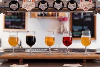Tasting flight of five craft beers from Burdigala Brewery in Bordeaux, displayed in glasses on a counter with brewery taps in the background.