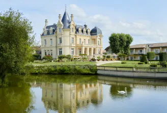 Grand Barrail Château Hotel in Bordeaux, a beige Second Empire castle with turrets reflected in a pond, surrounded by manicured gardens and outbuildings.