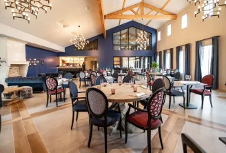Elegant dining room at Château Fage La Maison des Vignes in Bordeaux, featuring round wooden tables, black and red patterned chairs, cathedral ceiling with exposed beams, modern chandelier, and large windows.