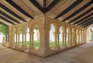 Cloister gallery of the Cordeliers in Bordeaux featuring Romanesque stone arcades with columns and exposed wooden beam ceiling