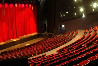 Interior of the National Theatre Bordeaux in Aquitaine showing rows of red seats facing a stage with red curtain and spotlight lighting.
