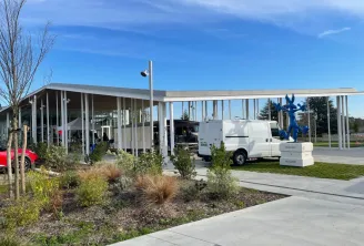 Vettiner Hall at Bouliac Market in Bordeaux, modern building with white columns, glazed canopy, blue statues and parked white van under clear sky
