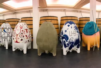 Collection of decorated oak barrels of various sizes and artistic designs arranged in a winemaking cellar at Château Larrivet Haut-Brion in Bordeaux.