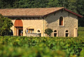 Classical stone building at Domaine de la Solitude in Bordeaux, featuring an orange arched door, rounded windows, red tile roof and vineyard vines in the foreground