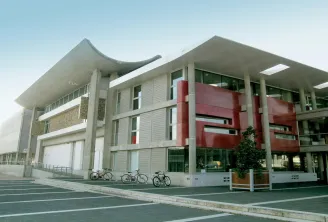 Modern building Le Carré in Saint-Médard-en-Jalles, Bordeaux, featuring contemporary concrete architecture with red accents, large columns, and bicycle parking.