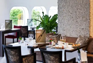 Elegant dining room with set tables, black and gold velvet chairs, arched windows overlooking greenery, floral and minimalist decor.