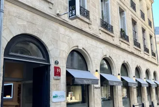 Facade of the Hôtel des Grands Hommes in Bordeaux, a stone building with ground-floor arcades, wrought-iron balconies on upper floors, and a Brit Hotel sign.