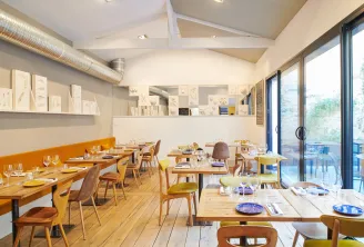 Modern interior of Zéphirine restaurant in Bordeaux featuring wooden tables, yellow and brown chairs, large glass windows, decorative wall shelves, and white vaulted ceiling.