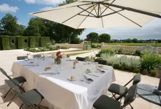 Outdoor dining table set under a white parasol in the gardens of Château Kirwan in Bordeaux, overlooking surrounding vineyards.