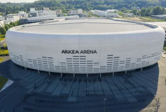 Aerial view of Arkea Arena, a modern white and grey rounded arena located in Floirac near Bordeaux, with parking areas and access plaza in the foreground.