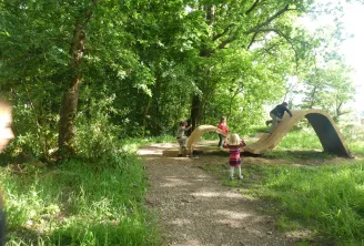 Children playing on a wooden natural play structure in a forest at Bois du Bouscat in Bordeaux, featuring a slide and climbing elements.