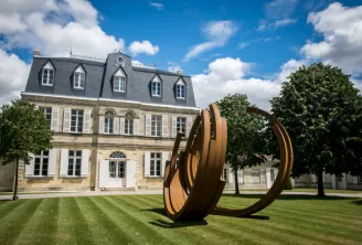 Château Malescasse in Bordeaux featuring classical stone architecture, slate mansard roof, and a contemporary rust-colored metal sculpture on manicured lawns