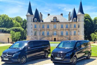 Two black Mercedes sedans parked in front of a Bordeaux-style château with towers and turrets, surrounded by greenery.