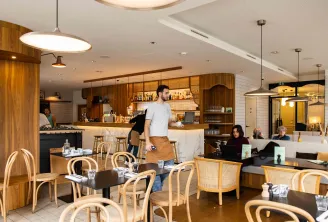 Interior of Bistrot Le Saint-Jean in Bordeaux featuring wooden counter, rattan chairs, seated guests, staff members, modern lighting, and warm atmosphere.