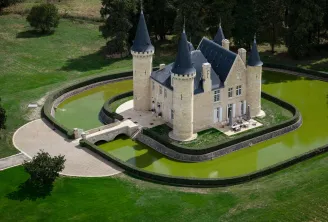 Aerial view of Château d'Agassac near Bordeaux, a medieval fortress with four conical towers surrounded by a water-filled moat, accessible via a stone bridge.
