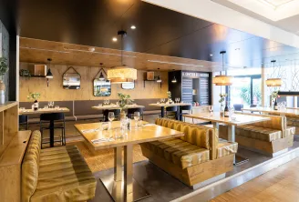 Contemporary dining room of Le Bistrot de Mériadeck in Bordeaux featuring wooden tables, golden booth seating, warm lighting, and natural wood wall panels.