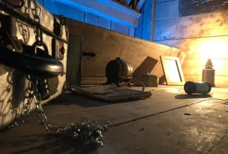 Interior of an escape room at Château de Lisennes in Bordeaux, featuring mysterious equipment including chains, a globe, metal objects, and dramatic yellow and blue lighting.