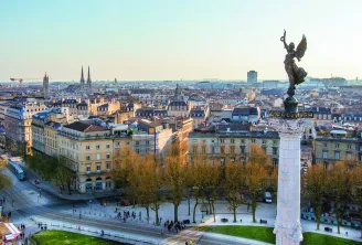 Panoramic view of Bordeaux featuring the Rostra Column on Place de la Victoire in the foreground, classical architecture, slate roofs and cathedral spires in the background