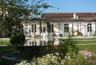 Château Chasse-Spleen in Bordeaux featuring a white mansion, pergola with climbing plants, reflecting pool, and landscaped gardens with flowers.