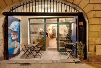 Storefront of Levain Le Vin wine shop in Bordeaux, featuring an outdoor terrace with folding chairs, illuminated display windows and blue promotional poster