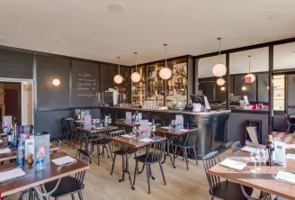 Interior of Café de l'Espérance in Bordeaux featuring wooden tables, black chairs, elegant bar counter, gold pendant lights, and sophisticated décor