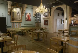 Elegant interior of Le Comptoir d'Etienne restaurant in Bordeaux featuring wooden tables and chairs, crystal chandelier, gilded mirror, wall paintings, and refined classical decoration.