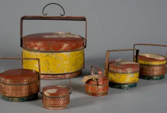 Collection of Chinese tiered lacquerware boxes in red and yellow with gold floral and geometric patterns, equipped with metal handles, displayed at the Bordeaux Museum of Ethnography.