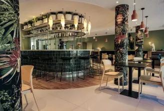 Elegant bar at Ibis Styles Bordeaux Lac Bruges hotel featuring a black counter, pendant lighting, decorative floral columns, modern seating, and olive green walls.