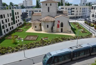 Aerial view of Saint-Vincent Church surrounded by modern residential buildings, with a tram in the foreground and landscaped gardens in Mérignac, Bordeaux.