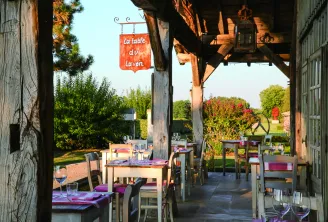Shaded terrace of La Table du Lavoir in Bordeaux with set tables, purple chairs and red signage, landscaped garden in the background