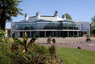 Modern Le Pin Galant building in Bordeaux featuring a glass facade, four cylindrical chimneys on the roof, surrounded by landscaped green areas and urban amenities.