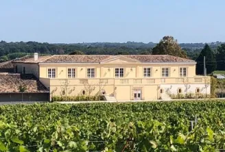 Château Larmande, a pale yellow wine estate with regularly spaced windows, surrounded by lush vineyards in the Bordeaux region