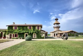 Exterior view of Château Smith Haut Lafitte in Bordeaux featuring ivy-covered main building, clock tower, manicured lawn and clear blue sky