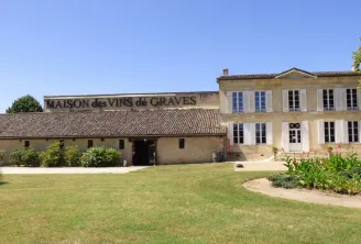 Facade of the Maison des Vins de Graves in Bordeaux, a stone building with tiled roof, surrounded by gardens and lawn.
