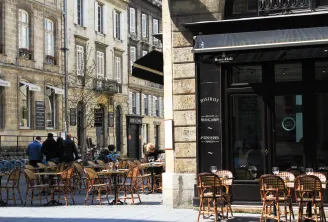 Outdoor terrace of a French bistro and Henri Abélé bakery on a paved street in Bordeaux, featuring rattan chairs and traditional stone facades in the Puy-Paulin district