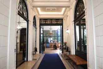 Elegant entrance hallway of a Bordeaux boutique hotel featuring white columns, ornate black doors, coffered ceiling with lighting, and blue carpet leading to the reception area
