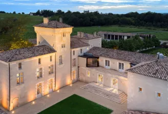 Aerial nighttime view of Château Lafaurie Peyraguey in Bordeaux, illuminated with its distinctive tower, tiled roofs and terraces, surrounded by vineyards.