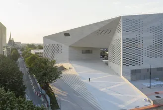 Exterior view of FRAC Nouvelle-Aquitaine MECA in Bordeaux, modern white building with perforated checkerboard facade, access stairs and large plaza, church visible in background