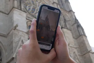 Hand holding a smartphone displaying an augmented reality app showing an orange-lit church, with Bordeaux cathedral in the background
