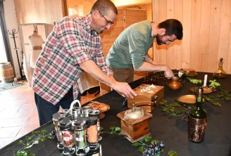 Two men participate in a wine tasting session in a wooden cellar. One pours wine into a glass while the other observes, surrounded by bottles, glasses and tasting accessories.