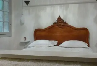 Elegant bedroom featuring a carved wooden bed with baroque details, pristine white linens, whitewashed walls, a window with panes, and minimalist décor in classic Bordeaux style.