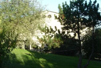 View of Château La Gontrie in Bordeaux with its white façade visible among trees, surrounded by green gardens and cypress trees.
