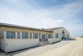 Front facade of Château de Rayne Vigneau in Bordeaux, stone building with white shutters, paved terrace and blue sky