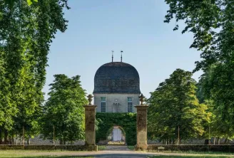 View of Château de Sales in Bordeaux featuring its distinctive blue dome, framed by a tree-lined avenue and bordered by stone porticos.