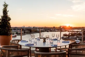 Sunset rooftop terrace with round dining table, rattan chairs, glassware and place settings overlooking Bordeaux cityscape and waterfront