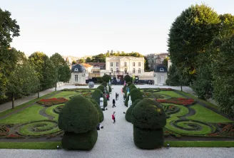 View of the courtyard at the Bernard Magrez Cultural Institute in Bordeaux featuring French formal gardens with manicured topiary and flower beds, and the main white building in the background