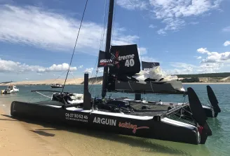 Black Arguin Xtreme 40 catamaran beached on sand with black sails, moored near Bordeaux with white cliffs in the background